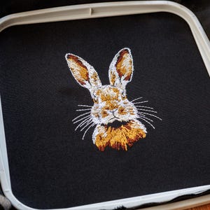 Peut inclure: Broderie repr&eacute;sentant un lapin brun avec du poil blanc sur le visage et la poitrine. Le lapin regarde directement le spectateur, les oreilles dress&eacute;es.
