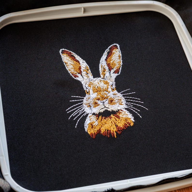 Peut inclure: Broderie repr&eacute;sentant un lapin brun avec du poil blanc sur le visage et la poitrine. Le lapin regarde directement le spectateur, les oreilles dress&eacute;es.