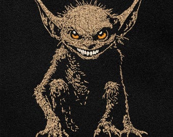 May include: Embroidered patch featuring a goblin-like creature with large ears, sharp teeth, and orange eyes. The patch is stitched in shades of tan and brown against a black background. The creature has a menacing grin and appears to be sitting.