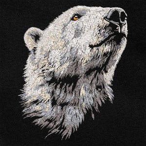 Peut inclure: Image brodée d'une tête d'ours polaire, rendue en nuances de blanc, de gris et de noir. La fourrure de l'ours est détaillée, avec un accent sur la texture et la direction des brins. L'œil de l'ours est d'une couleur ambre chaude, et le fond est noir uni.