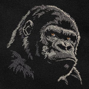 以下が含まれることがあります： ゴリラの顔の白黒刺繍のアップ。ゴリラは口を閉じ、目を直接見ているため、真剣な表情をしている。