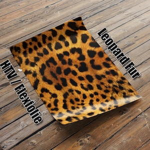 Puede incluir: Una lámina de vinilo termoadhesivo (HTV) o plancha de transferencia con estampado de leopardo. El vinilo es de color dorado y negro y tiene un patrón de piel de leopardo realista. El texto "Leopard Fur" y "HTV / Flexfolie" está escrito en la lámina.