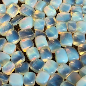 May include: A collection of tumbled opalite stones. The stones are a milky white colour with iridescent blue and green hues. The stones are smooth and polished.
