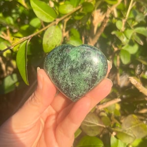 Peut inclure: Une pierre en forme de cœur verte et noire avec un motif moucheté. La pierre est tenue dans une main.