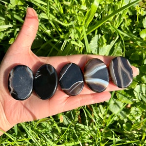 May include: Five black and white agate palm stones. The stones are smooth and polished, with a variety of patterns.