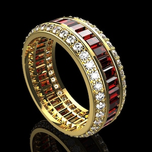 Puede incluir: Un anillo de oro con una banda de piedras rojas rectangulares y una fila de pequeñas piedras blancas redondas. El anillo está sobre un fondo negro, creando un contraste llamativo.
