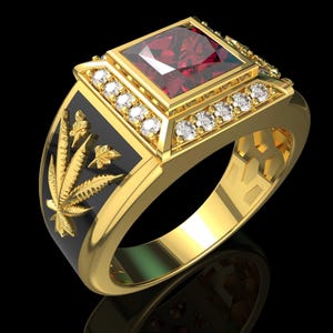 May include: A gold ring featuring a square-cut deep red gemstone at the center, surrounded by small clear stones. The sides of the band are inlaid with black enamel and feature a raised gold cannabis leaf design on each side of the ring.