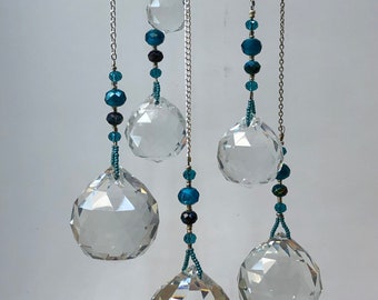 May include: A crystal suncatcher with five clear crystal balls hanging from silver chains. Each chain is adorned with teal blue beads.