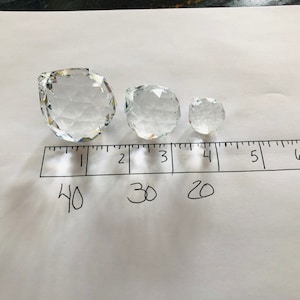 May include: Three clear crystal decorative spheres of varying sizes are arranged on a white surface next to a ruler. The largest sphere is approximately 4 inches in diameter, the middle sphere is 3 inches, and the smallest is 2 inches.
