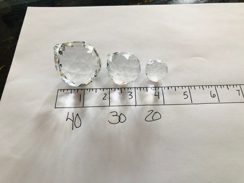 May include: Three clear crystal decorative spheres of varying sizes are arranged on a white surface next to a ruler. The largest sphere is approximately 4 inches in diameter, the middle sphere is 3 inches, and the smallest is 2 inches.
