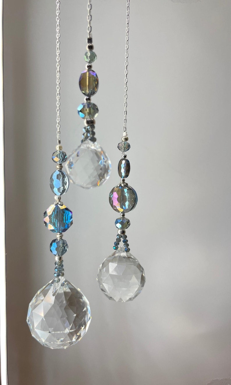 May include: Three hanging crystal suncatchers with iridescent beads and faceted crystal balls. The suncatchers are suspended by silver chains and feature a variety of blue and clear beads. The crystal balls are multi-faceted.