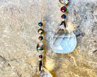 May include: Two crystal prisms hanging from silver chains with iridescent beads. The beads are a mix of clear, black, and iridescent green, purple, and blue.