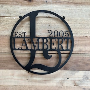 May include: Black metal circle sign with the text "EST 2005 LAMBERT" and a large letter "L" in the center.