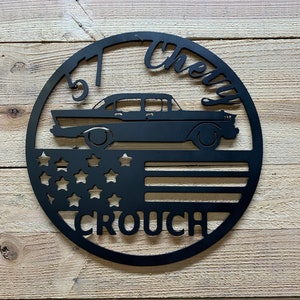 Puede incluir: Un letrero de metal negro con la silueta de un Chevrolet de 1957, una bandera estadounidense y el texto "Cherry Crouch".