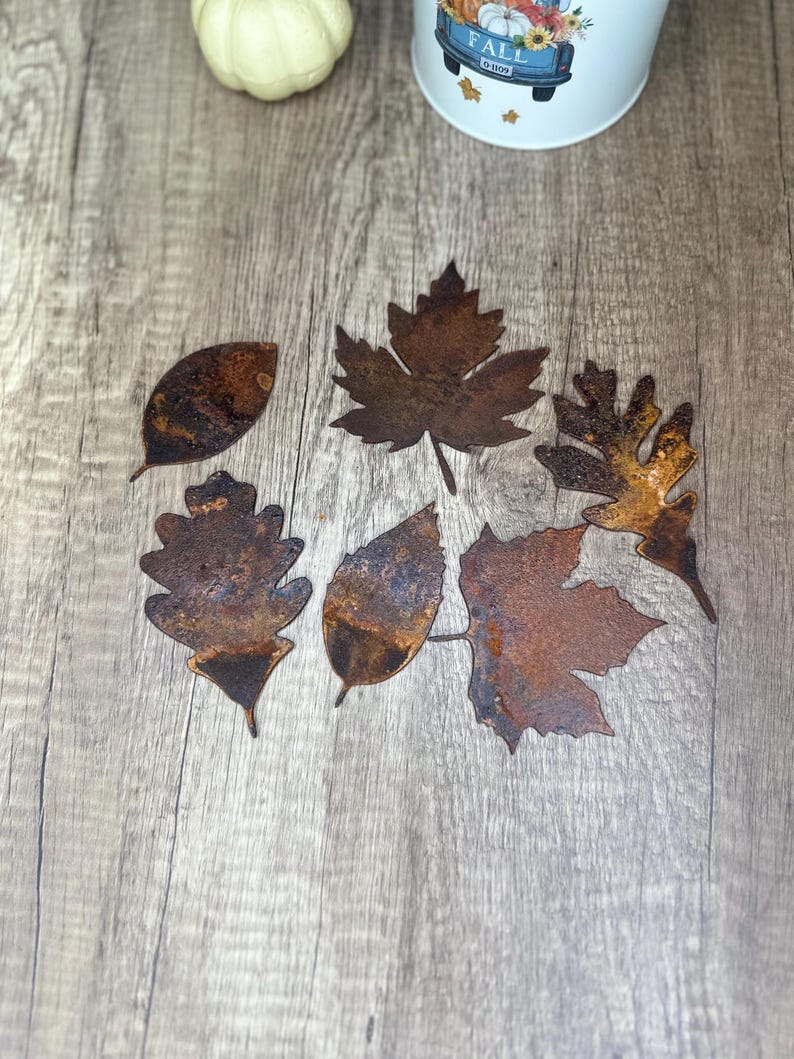 May include: Six rusty metal leaf cutouts in various shapes, including maple, oak, and simple leaf shapes, on a woodgrain surface.