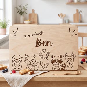 Peut inclure: Une planche &agrave; d&eacute;couper rectangulaire en bois clair avec un motif grav&eacute; au laser repr&eacute;sentant cinq animaux des bois : une loutre, un renard, un lapin, un raton laveur et un cerf. Le texte "Hier kr&uuml;melt Ben" est grav&eacute; au-dessus avec un c&oelig;ur.
