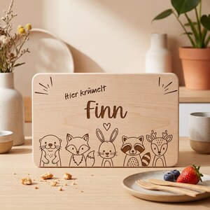Peut inclure: Une planche &agrave; d&eacute;couper rectangulaire en bois clair avec un motif grav&eacute; au laser repr&eacute;sentant cinq animaux de la for&ecirc;t : une loutre, un renard, un lapin, un raton laveur et un cerf. Le texte "Hier kr&uuml;melt finn" est grav&eacute; avec un petit c&oelig;ur.