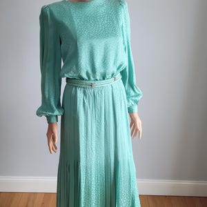 May include: A mint green dress with a pleated skirt and a patterned bodice. The dress has long sleeves and a fitted waist.