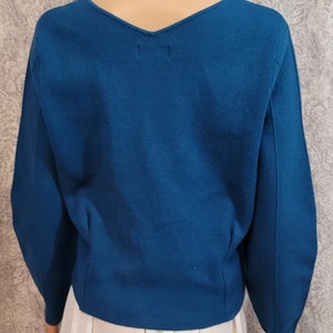 Pu&ograve; includere: Un maglione blu turchese con scollo a V e maniche lunghe. Il maglione &egrave; realizzato in un tessuto morbido e lavorato a maglia.
