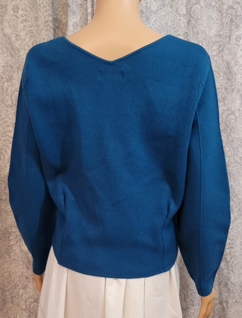 Pu&ograve; includere: Un maglione blu turchese con scollo a V e maniche lunghe. Il maglione &egrave; realizzato in un tessuto morbido e lavorato a maglia.