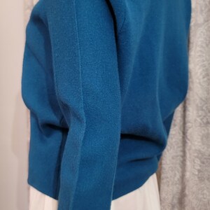 Pu&ograve; includere: Un maglione a maniche lunghe blu turchese con scollo a V. Il maglione &egrave; realizzato in un tessuto morbido e lavorato a maglia.