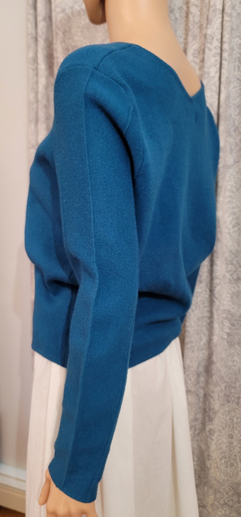 Pu&ograve; includere: Un maglione a maniche lunghe blu turchese con scollo a V. Il maglione &egrave; realizzato in un tessuto morbido e lavorato a maglia.