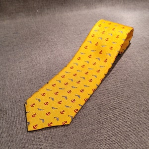 May include: A yellow silk tie with a pattern of red anchors and blue dolphins.