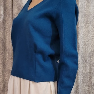 Pu&ograve; includere: Un maglione a maniche lunghe blu turchese con scollo a V.