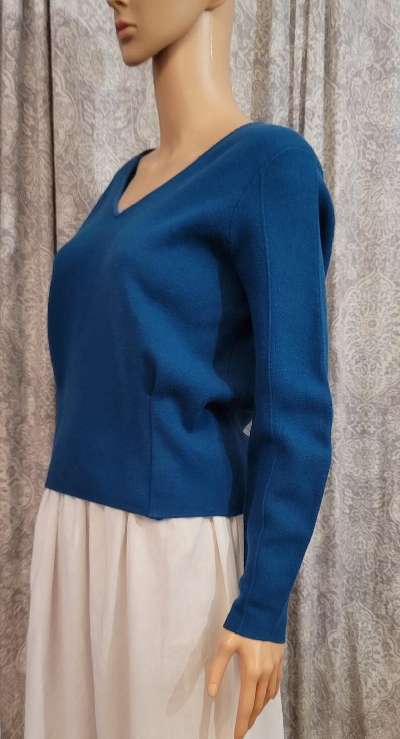 Pu&ograve; includere: Un maglione a maniche lunghe blu turchese con scollo a V.