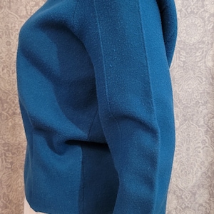 Pu&ograve; includere: Un maglione blu teal a maniche lunghe con scollo rotondo. Il maglione &egrave; realizzato in un tessuto morbido e lavorato a maglia.