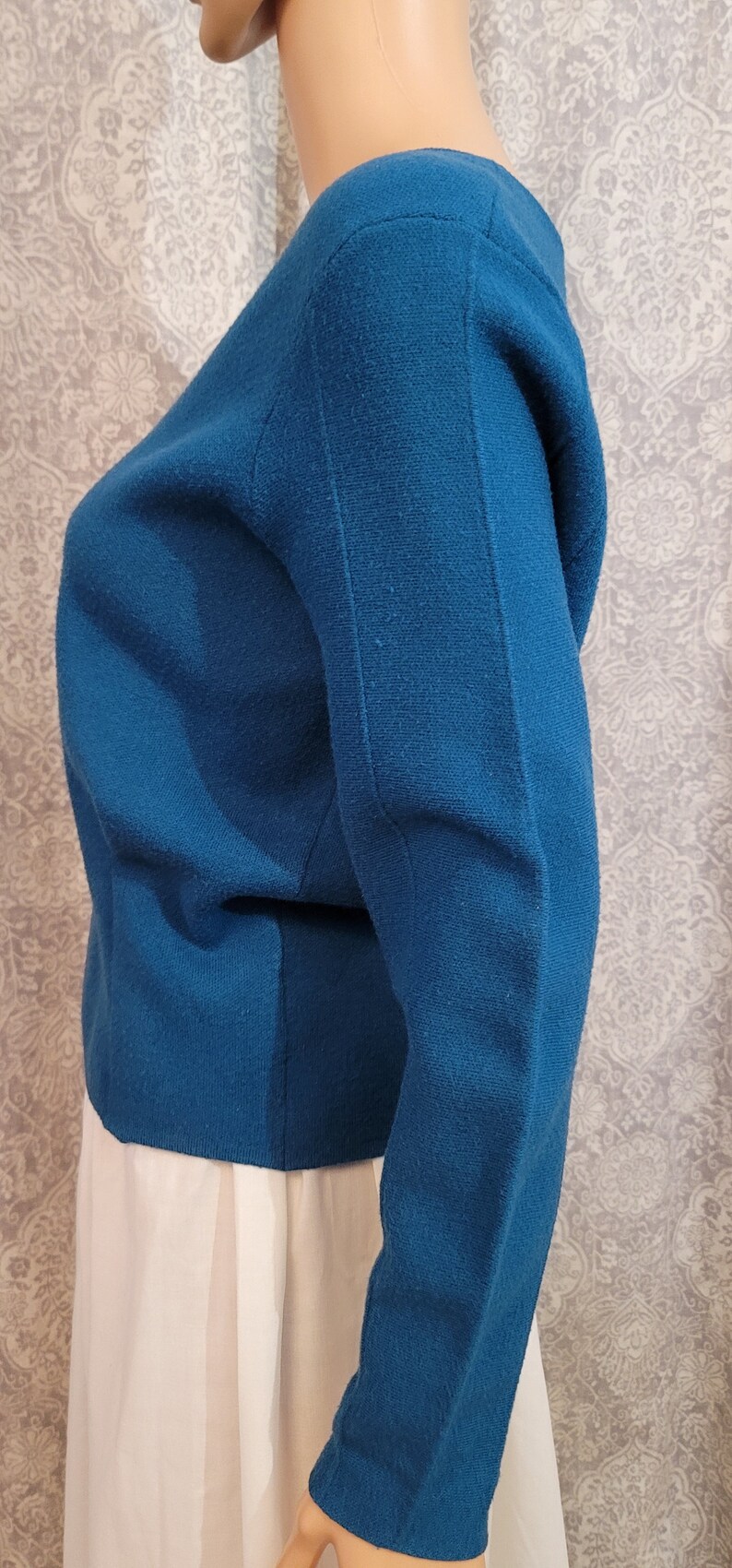 Pu&ograve; includere: Un maglione blu teal a maniche lunghe con scollo rotondo. Il maglione &egrave; realizzato in un tessuto morbido e lavorato a maglia.