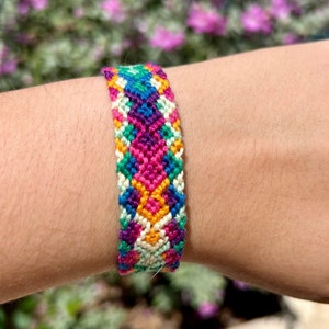 May include: A colorful friendship bracelet with a geometric pattern in shades of pink, green, blue, yellow, and white.
