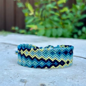 May include: A blue, yellow, and black friendship bracelet with a chevron pattern.
