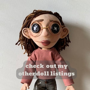 May include: A handmade doll with button eyes, wearing round wire-rimmed glasses. The doll has brown dreadlocks, a pink shirt, and gray pants. Text on the image reads "check out my other doll listings."