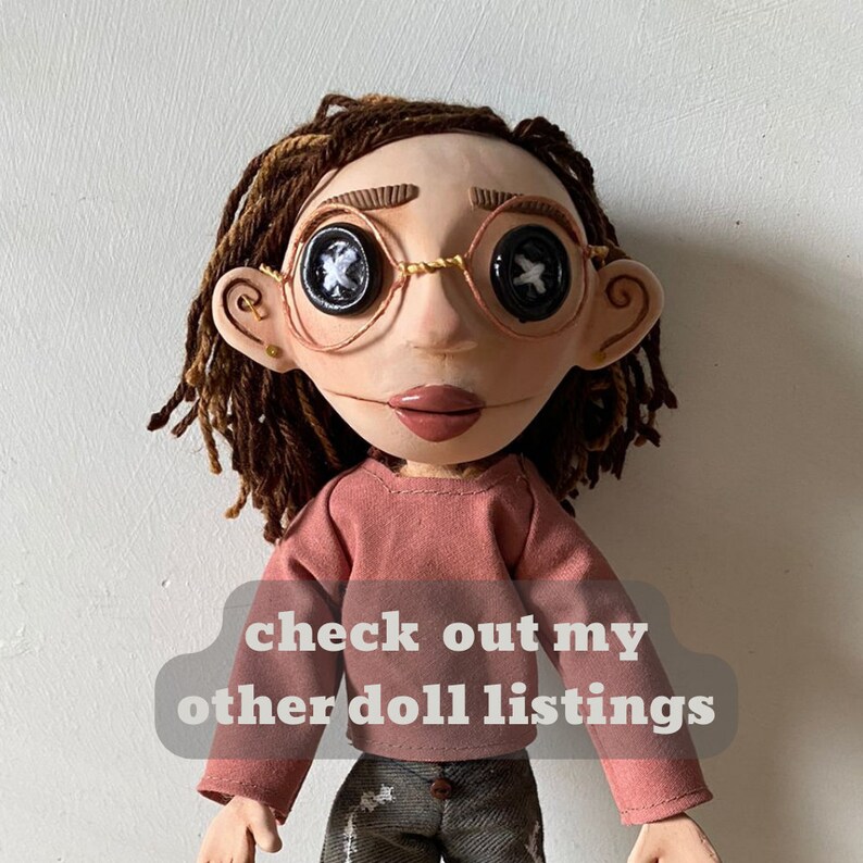May include: A handmade doll with button eyes, wearing round wire-rimmed glasses. The doll has brown dreadlocks, a pink shirt, and gray pants. Text on the image reads "check out my other doll listings."