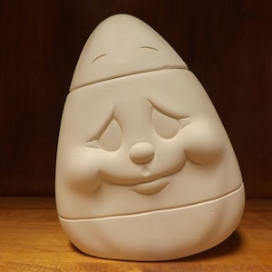 May include: An off-white ceramic egg-shaped container with a smiling face. The container has a lid and is designed with a face featuring closed eyes, a small nose, and a curved mouth. Suitable for storage or decorative purposes.