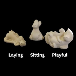 May include: Three ceramic figurines of a small animal, each in a different pose: laying down, sitting up, and playfully rolling on its back.
