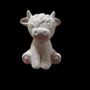 May include: A white ceramic Highland cow ornament with a shaggy coat, small horns, and a downcast expression. The cow is seated, with its paws showing. The background is plain black.