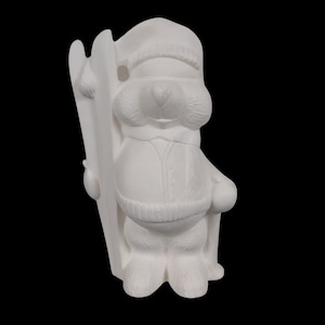 Puede incluir: Figurilla de cerámica blanca de un oso con un sombrero y sosteniendo bastones de esquí. El oso está de pie sobre un par de esquís.