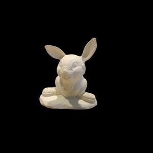 May include: A white ceramic bunny figurine with long ears and a smiling face. The bunny is sitting on a small, textured base. The figurine is unpainted and ready for customization.
