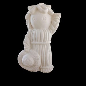Puede incluir: Figura de cerámica color crema de una niña con un gorro y un sombrero. La figura tiene un diseño detallado, que incluye un cinturón de cuerda y una falda con volantes. El fondo es negro liso.