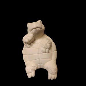 May include: A white ceramic turtle figurine with a textured shell and a detailed face. The turtle is sitting up on its hind legs with its front legs tucked in.