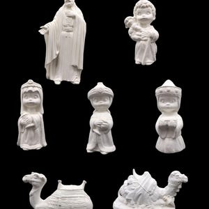 Puede incluir: Conjunto de figuras de cerámica sin pintar, que incluyen un hombre con túnica, un niño con un cordero, tres figuras con tocados y dos camellos. Fondo negro.