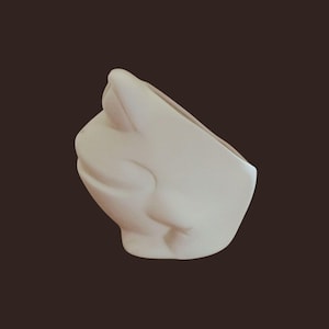Puede incluir: Una maceta de cerámica de color crema con un diseño abstracto único. La maceta tiene una base redondeada y una abertura inclinada, con una superficie texturizada. La forma general recuerda a una cara o forma estilizada.