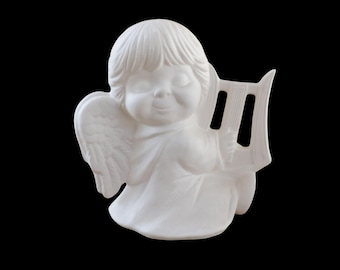 Może przedstawiać: Biała ceramiczna figurka anioła z zamkniętymi oczami i delikatnym uśmiechem. Anioł ma skrzydło po jednej stronie i trzyma harfę. Figurka jest umieszczona na czarnym tle.