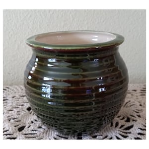 May include: A green and brown ceramic planter with a smooth, glossy finish. The planter has a rounded shape and a wide opening.