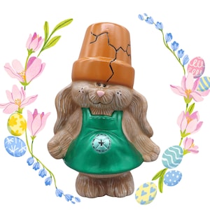 May include: A ceramic Easter bunny figurine wearing a green dress and a cracked orange flower pot on its head. The bunny is surrounded by a wreath of pink and blue flowers and colorful Easter eggs.