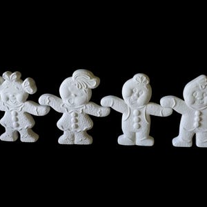 Könnte beinhalten: Vier weiße Keramik-Lebkuchenmännchen-Figuren mit ausgestreckten Armen, vor schwarzem Hintergrund. Jede Figur hat eine einzigartige Frisur und Knopfd details auf ihrer Kleidung. Die Figuren stehen in einer Reihe.