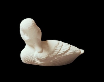Könnte beinhalten: Weiße Keramik-Entenfigur mit detaillierten Federn. Die Ente liegt auf der Seite mit dem Kopf nach hinten gedreht.