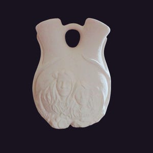 May include: White ceramic vase with two openings and a handle. The vase is decorated with a relief sculpture of two women's faces.